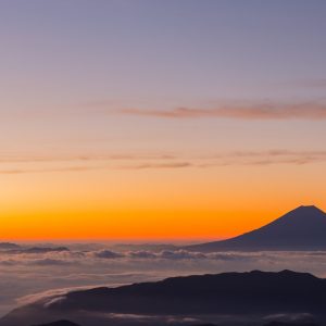 Orange sunset, clear sky, mountain rising above clouds.